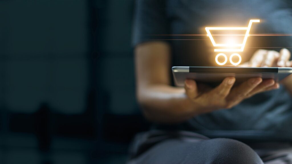hand holding laptop with graphic of shopping cart on top