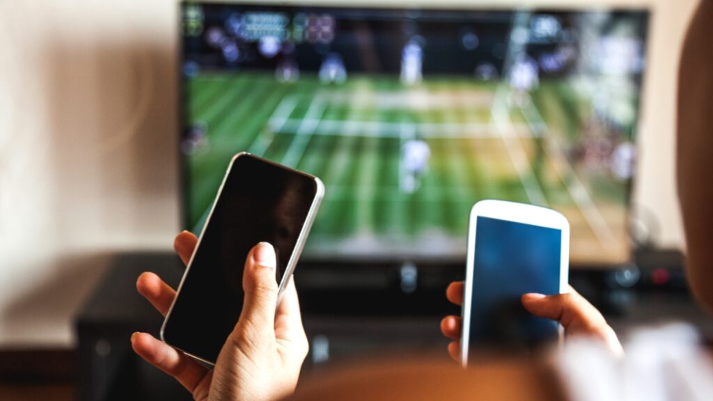 two people holding phones while watching sports