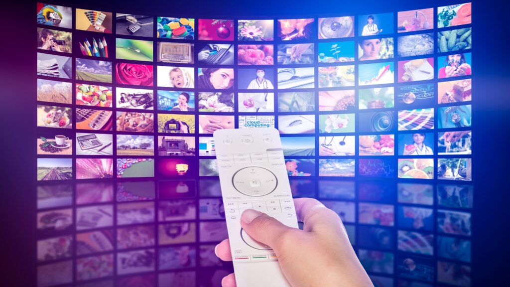 hand with remote pointed at wall of screens