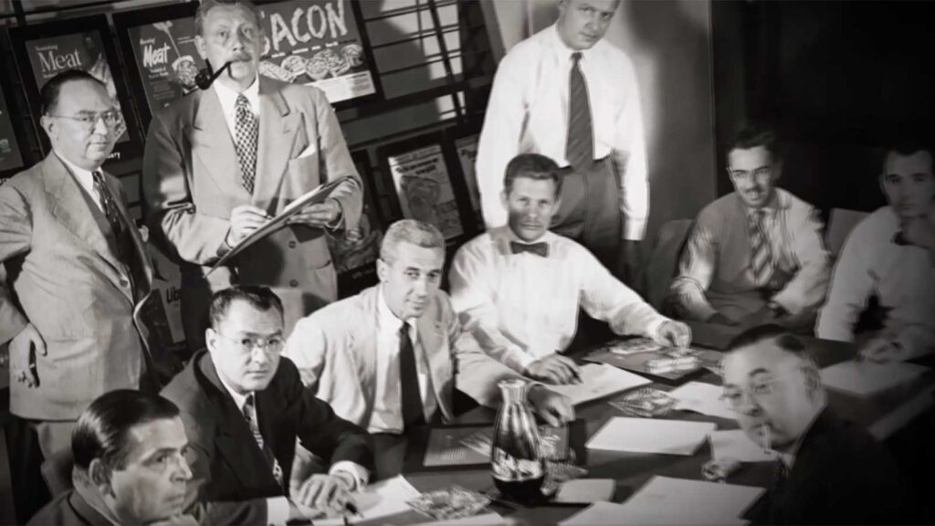 1950s black and white photo of white men sitting around conference table