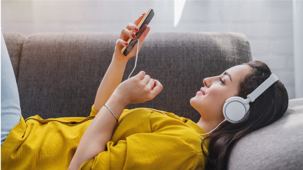 Side view of young woman listening to music online on smartphone in headphones