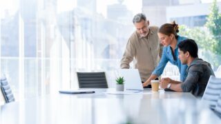 A Hispanic business leader discussing work with 2 employees