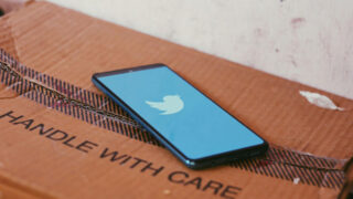 Phone displaying Twitter atop of a box that reads Handle With Care