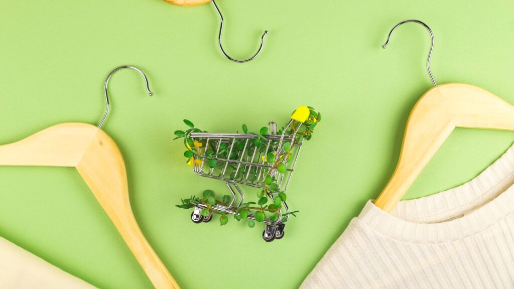 Shopping cart entwined with plants on green background among hangers. Sustainable eco lifestyle.