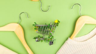 Shopping cart entwined with plants on green background among hangers. Sustainable eco lifestyle.