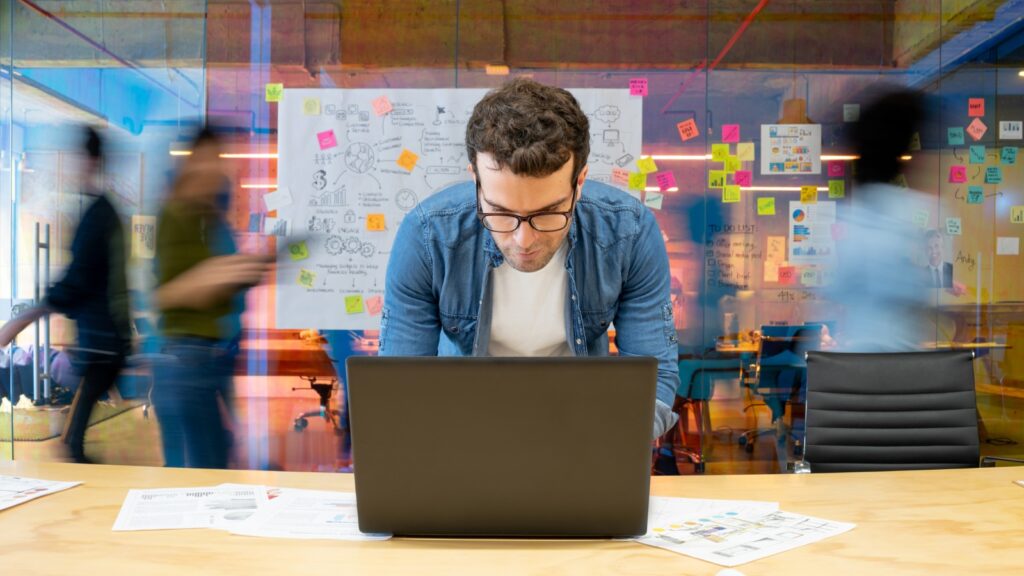 Man working at a creative office using his computer and people moving at the background stock photo